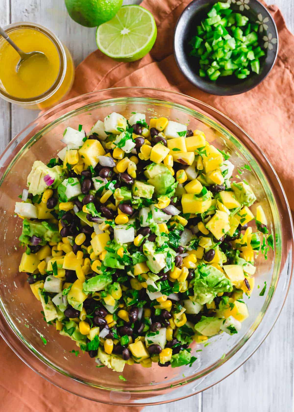 Black bean salad with mango in a glass bowl with dressing in glass jar on the side.