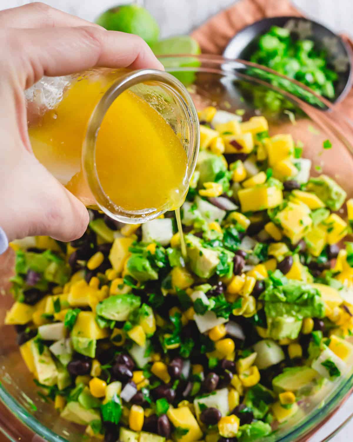 Pouring lime vinaigrette over a mango black bean salad.