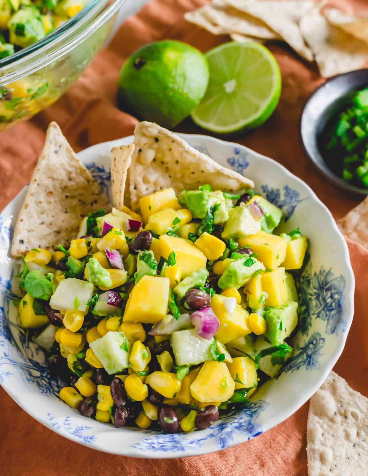 Mango, black beans, red onion, corn, jicama, avocado and cilantro salad in a bowl with tortilla chips.