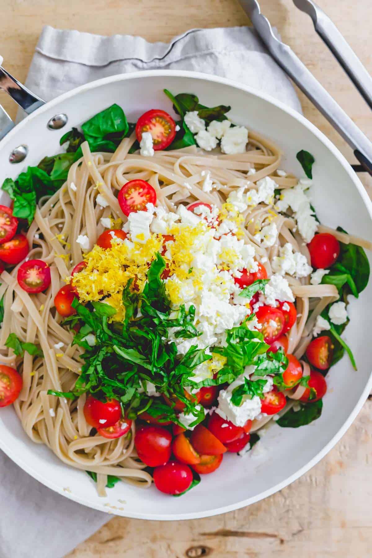 Lemon feta spinach pasta in a white skillet with tongs on the side.