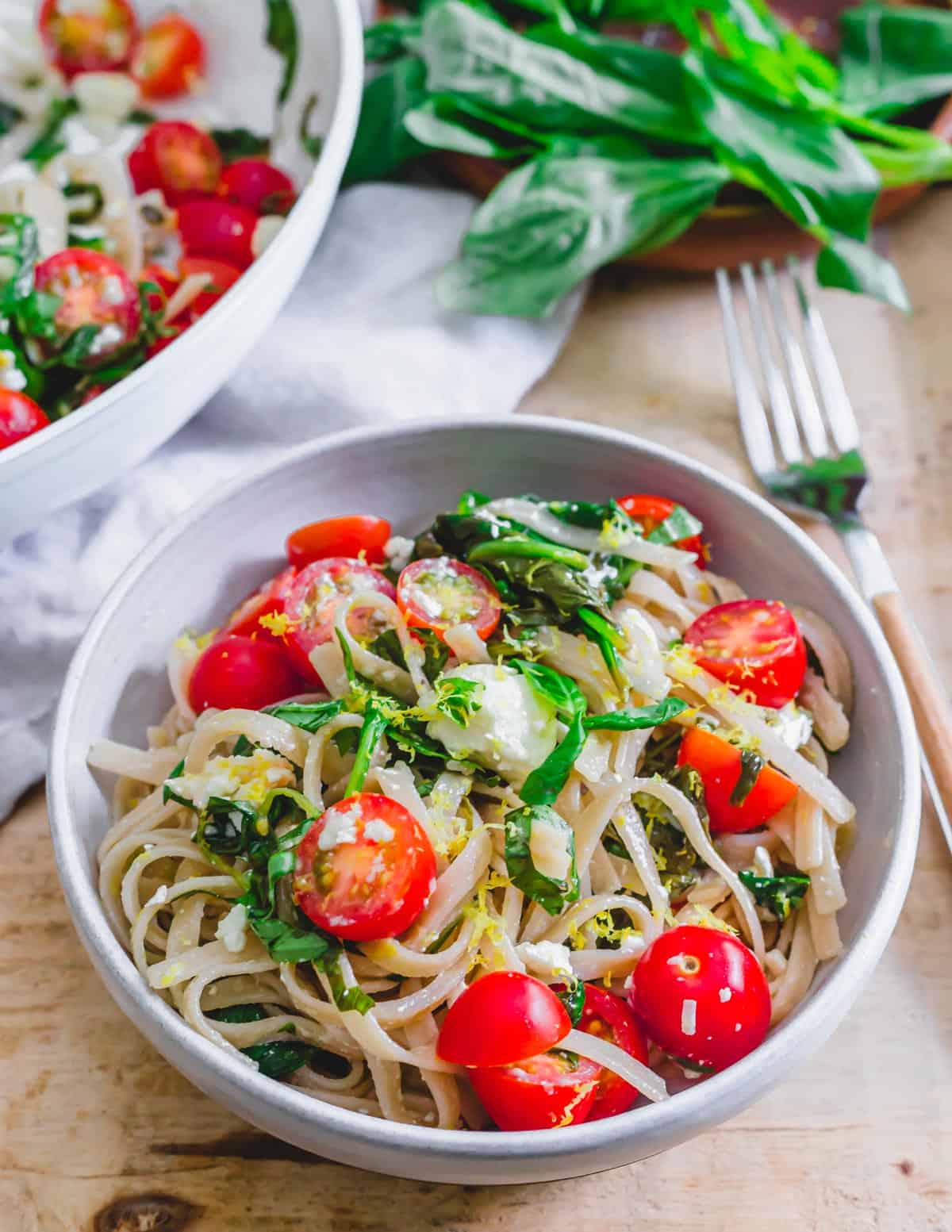 Lemon spinach feta pasta with cherry tomatoes in a white bowl on a wooden surface.
