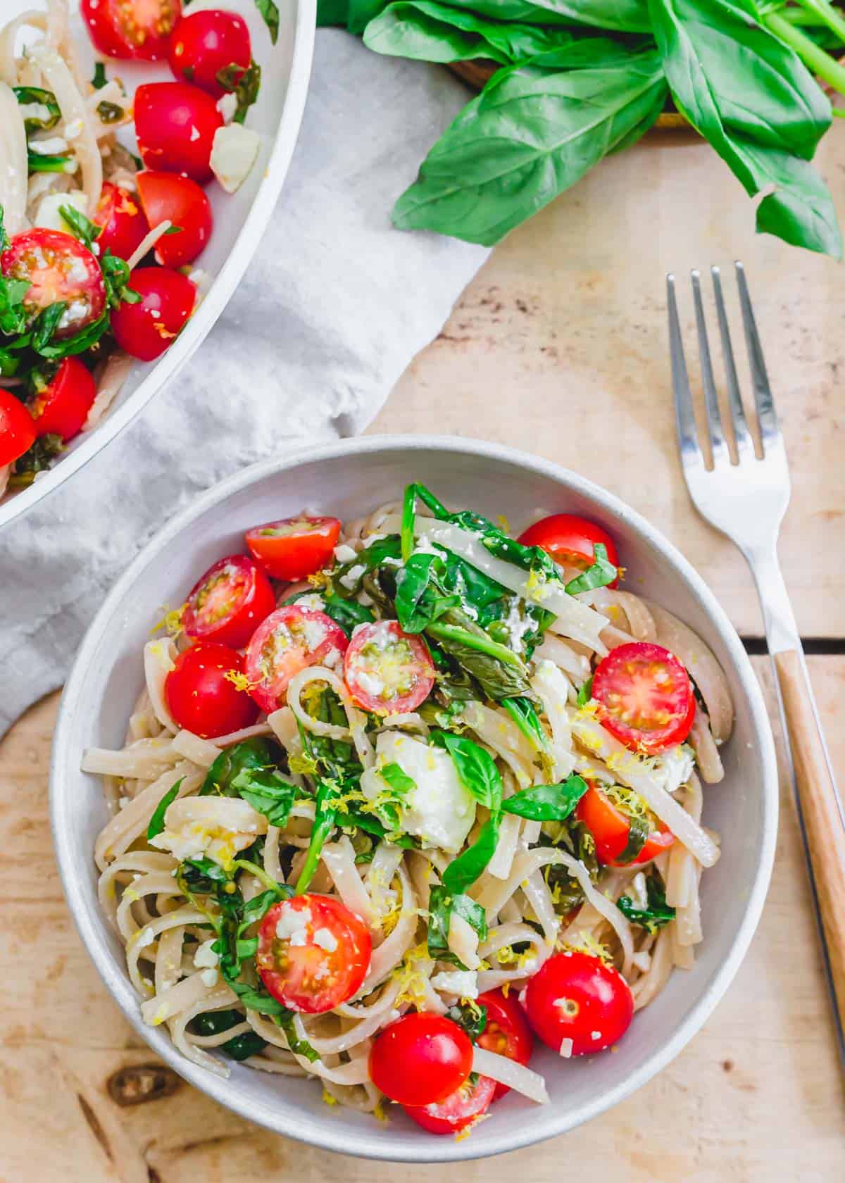 Lemon spinach feta pasta. in a bowl with fresh basil leaves and a fork to the side.