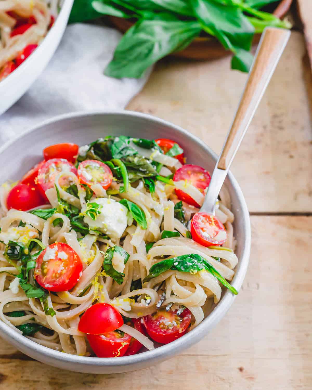 Pasta with spinach, tomatoes, feta and lemon in a bowl with a fork.