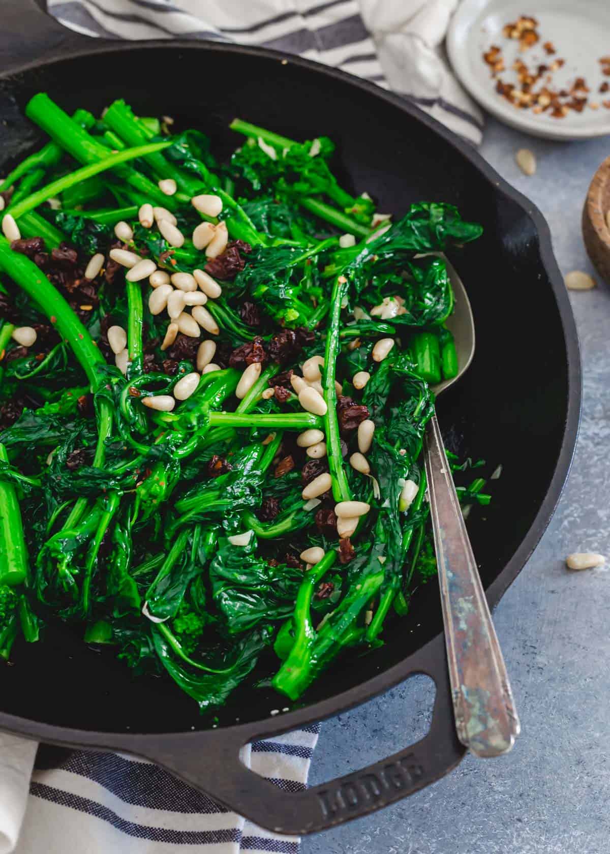 Broccoli rabe sautéed with garlic, red pepper flakes and olive oil in a skillet with a metal spoon.