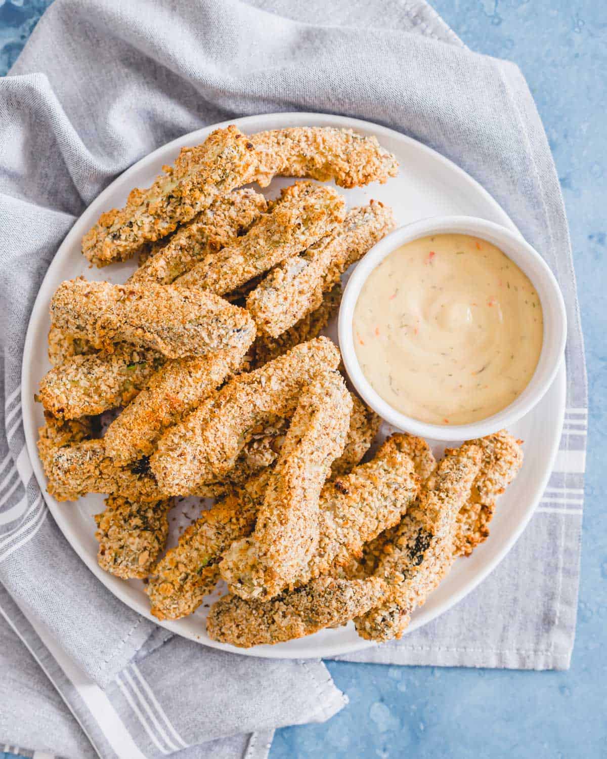 Healthy vegan "fried" zucchini fries made in the oven on a plate with dipping sauce on the side.