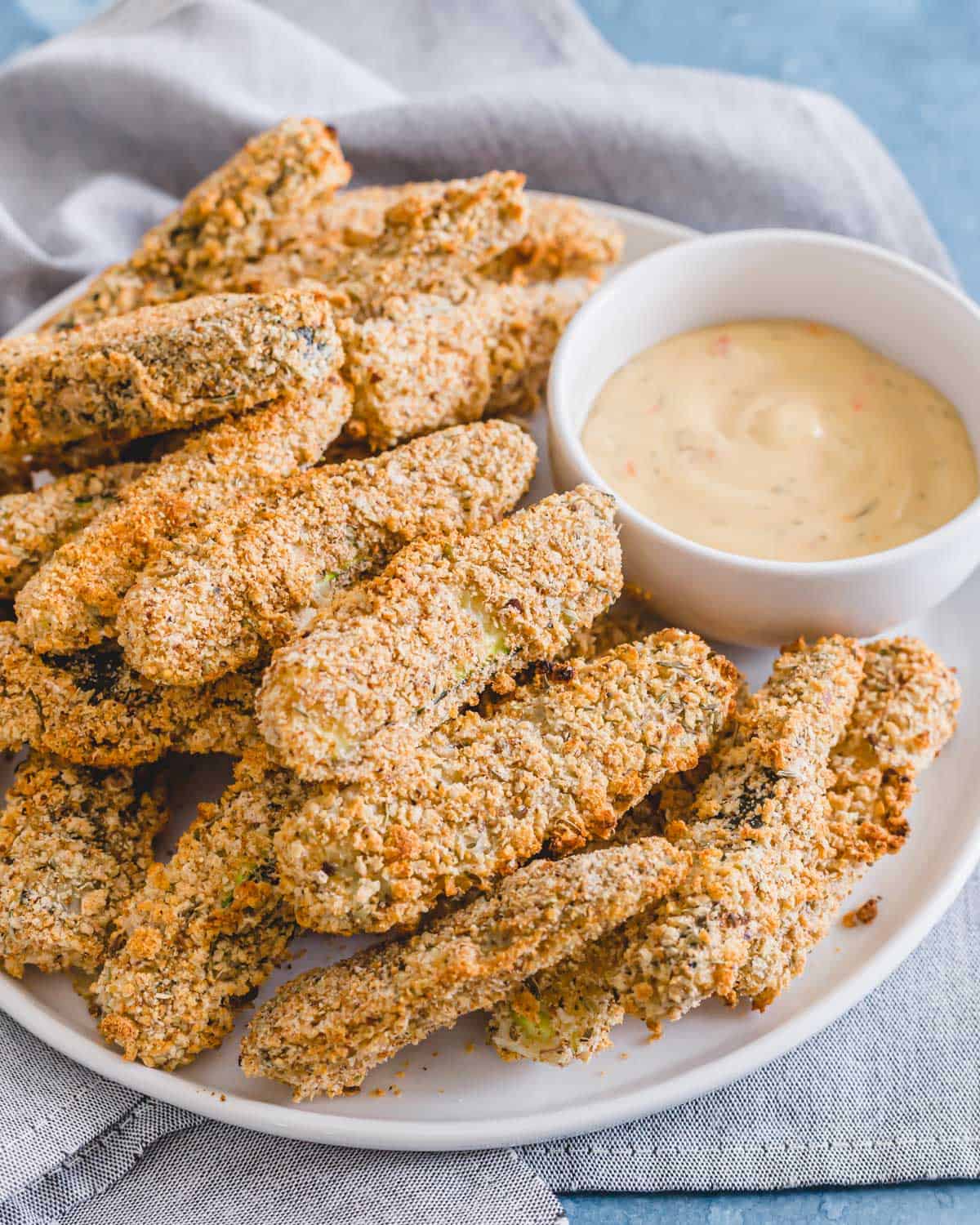 Vegan zucchini fries on a plate with dipping sauce in a white bowl.