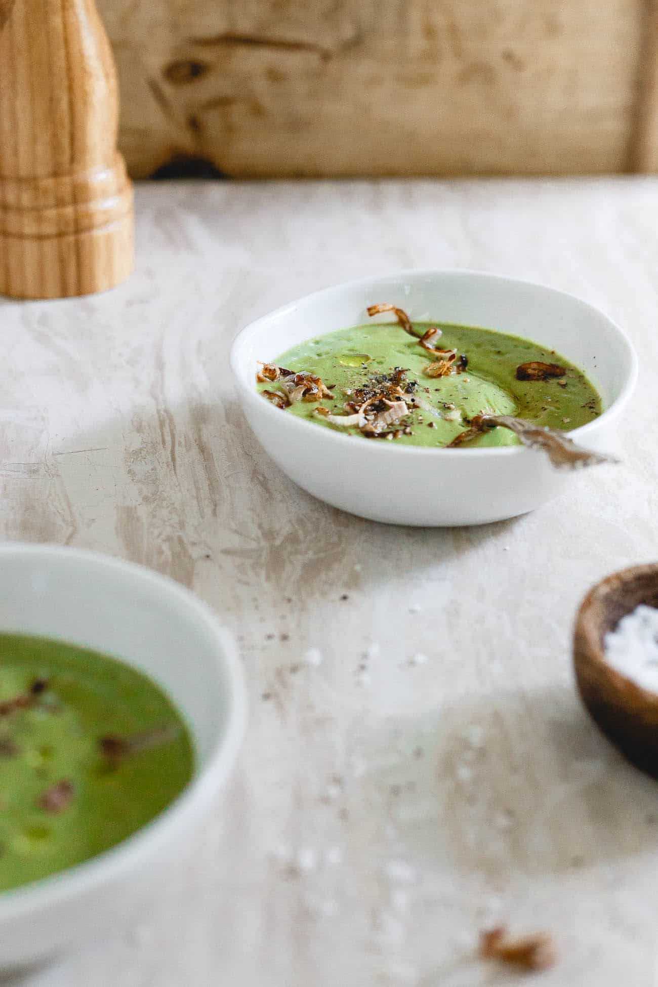 A white bowl full of vegan and vegetarian broccoli soup topped with crispy shallots and black pepper.