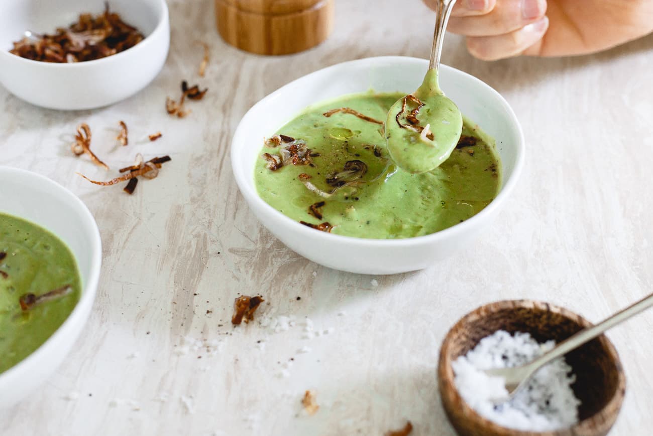 A bowl of creamy vegan broccoli soup with a silver spoon.