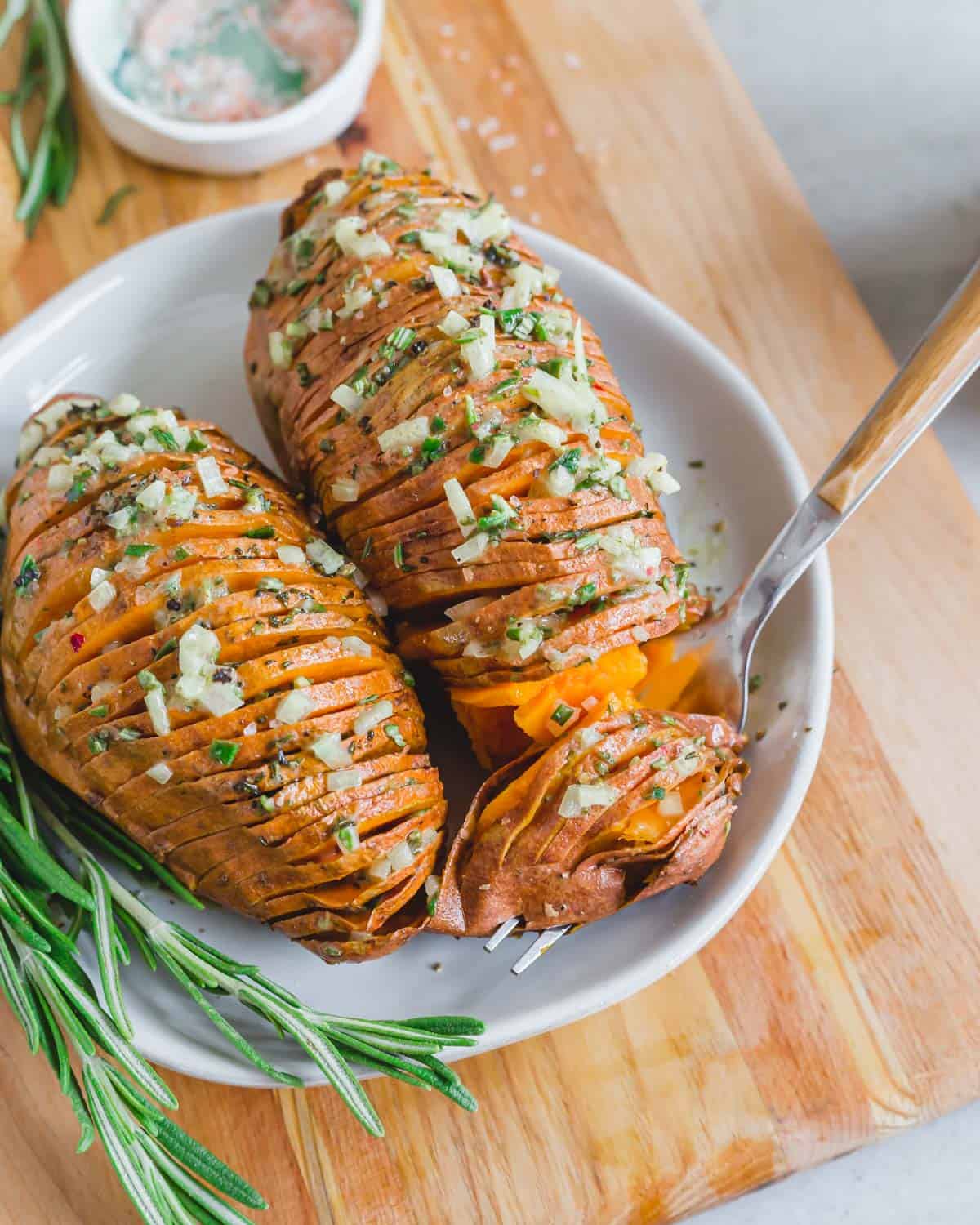 Vegan hasselback sweet potatoes with rosemary mustard shallot dressing on a plate with a fork.