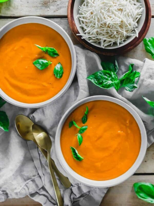 Two bowls of tomato soup with basil on a wooden table.