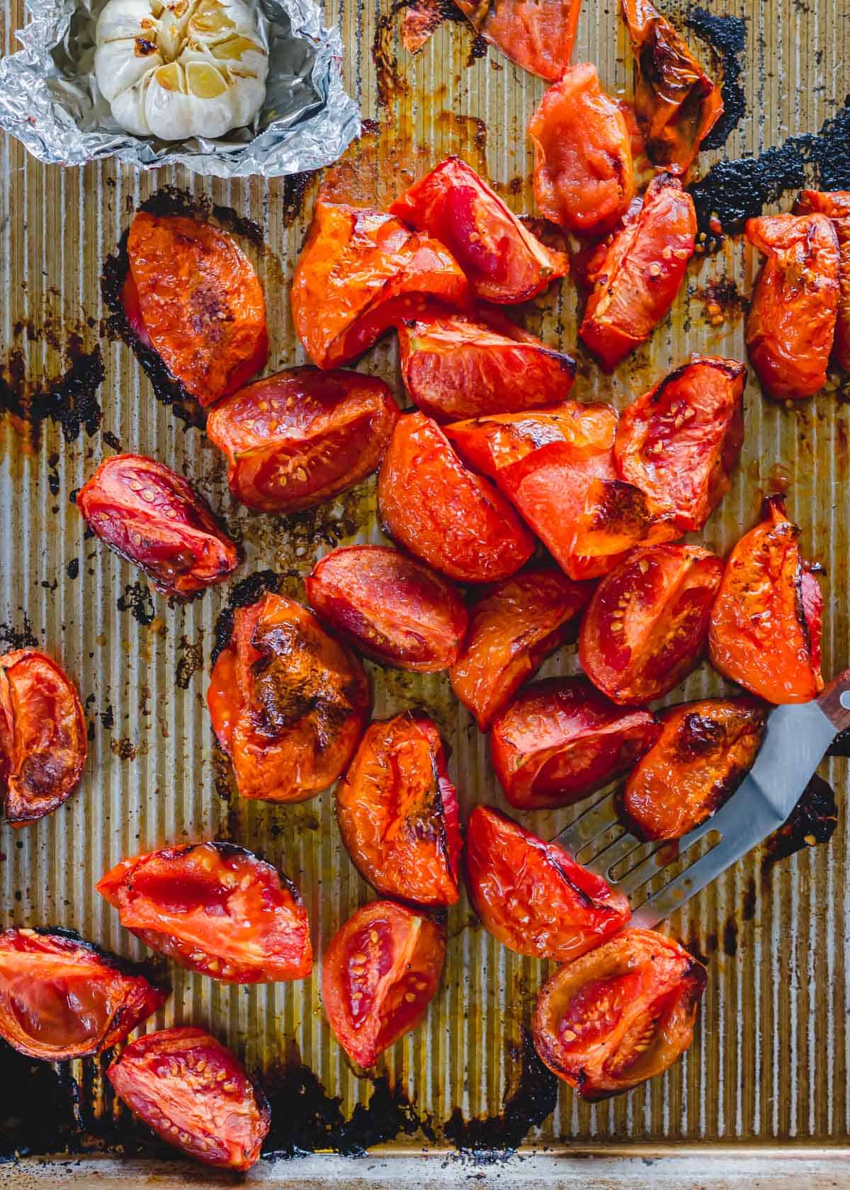 Roasted tomatoes and roasted head of garlic on a baking sheet.