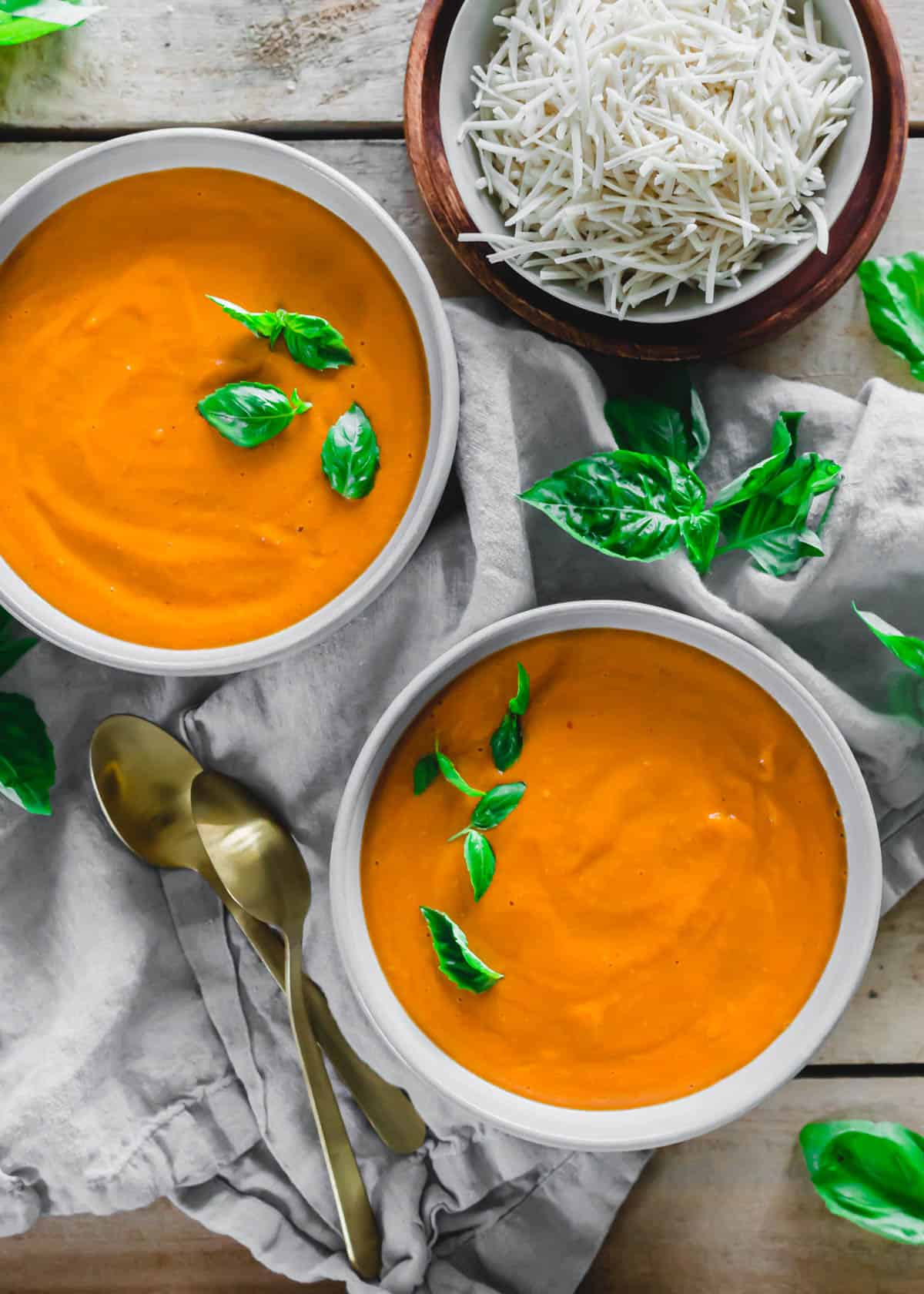 Roasted tomato soup in bowls with fresh basil garnish.