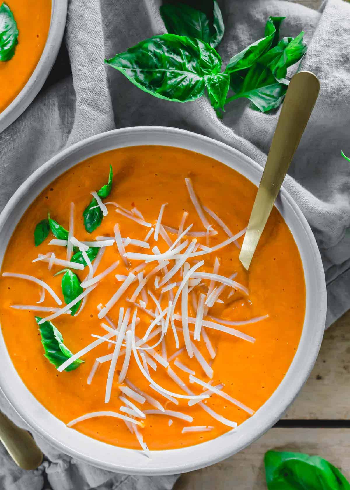 Creamy tomato soup recipe with roasted garlic in a bowl with a spoon garnished with parmesan cheese.