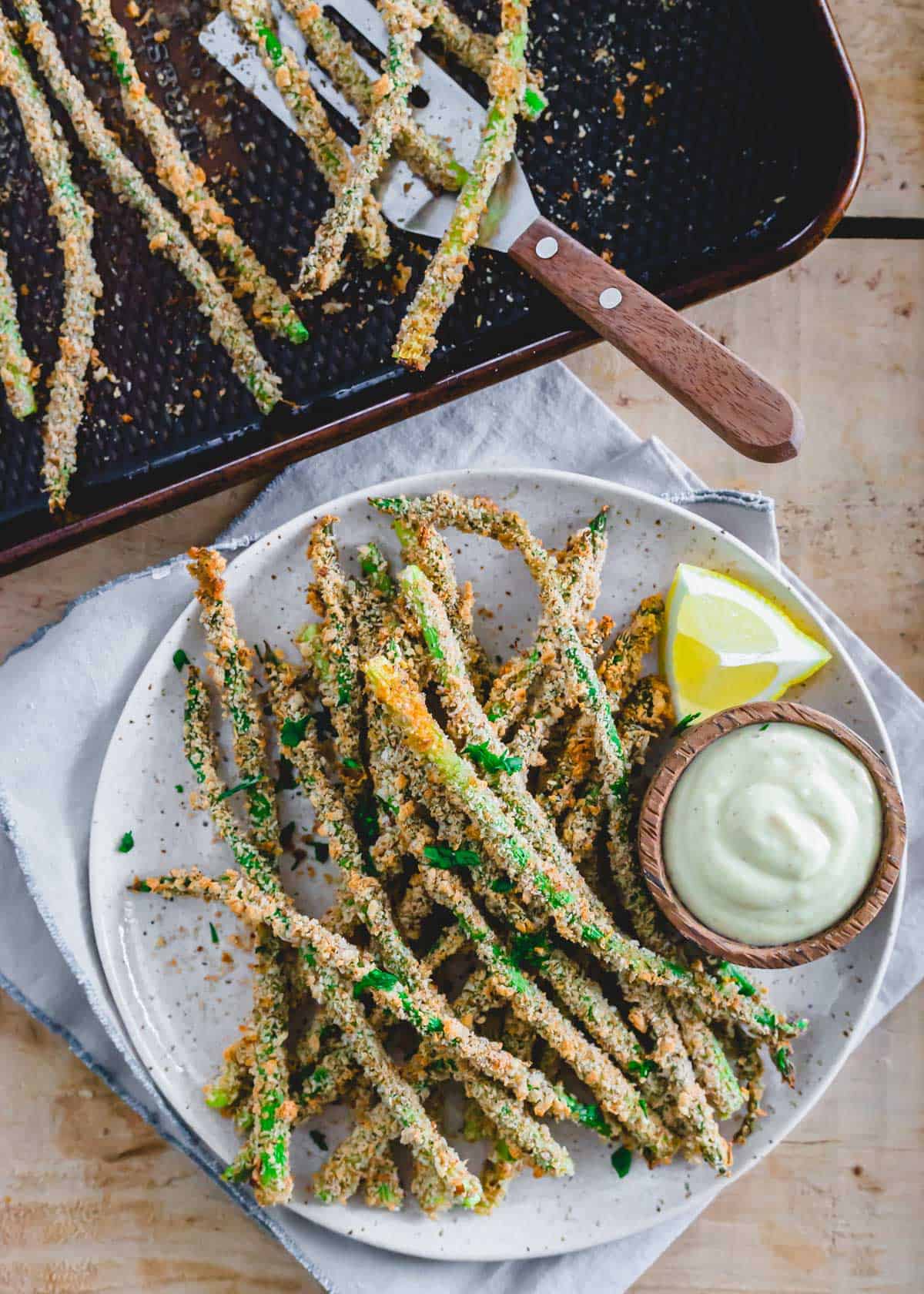 Crispy asparagus fries garnished with parsley on a plate with lemon dijon dipping sauce.