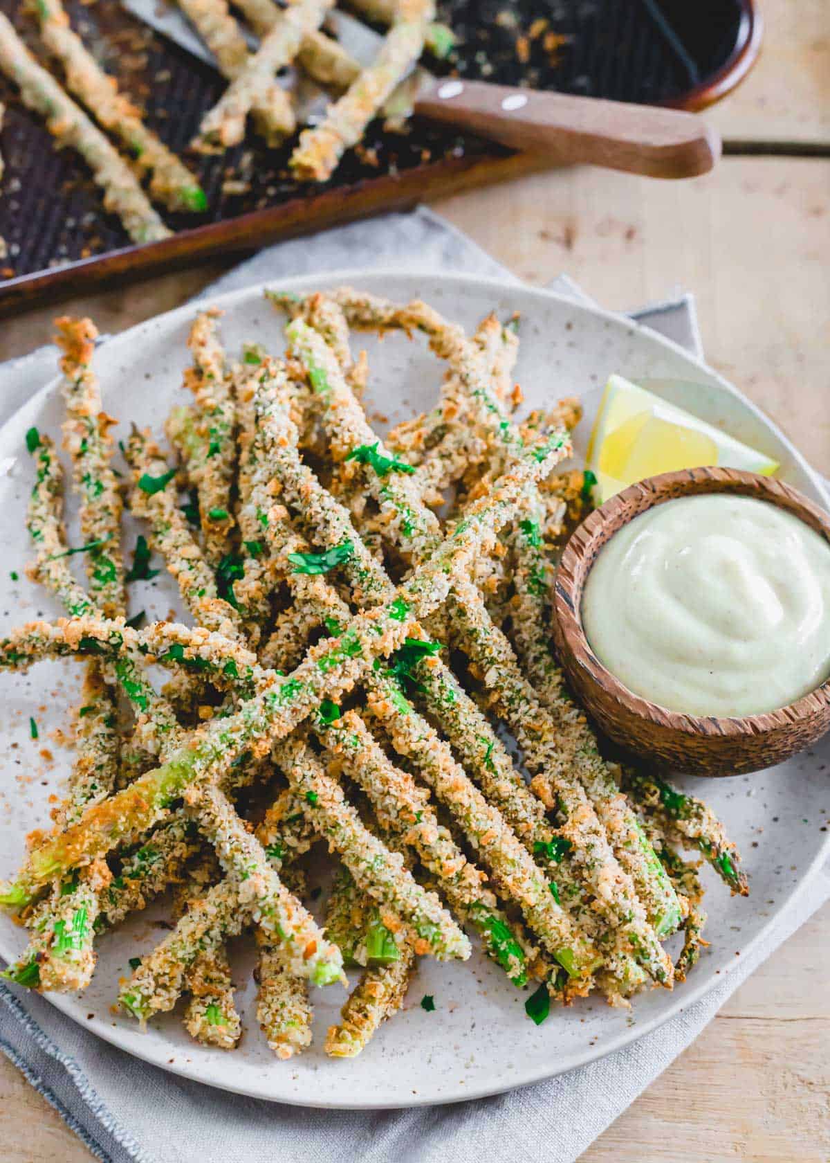 Crispy baked asparagus fries on a plate with lemon wedge and dipping sauce.