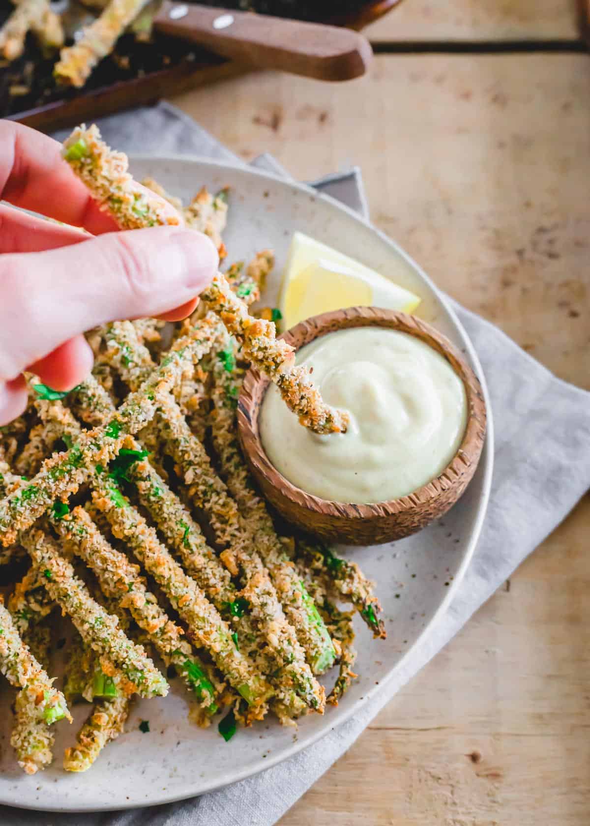 Gluten-free and vegan asparagus fries made in the oven or air fryer being dipped into lemon dijon sauce.