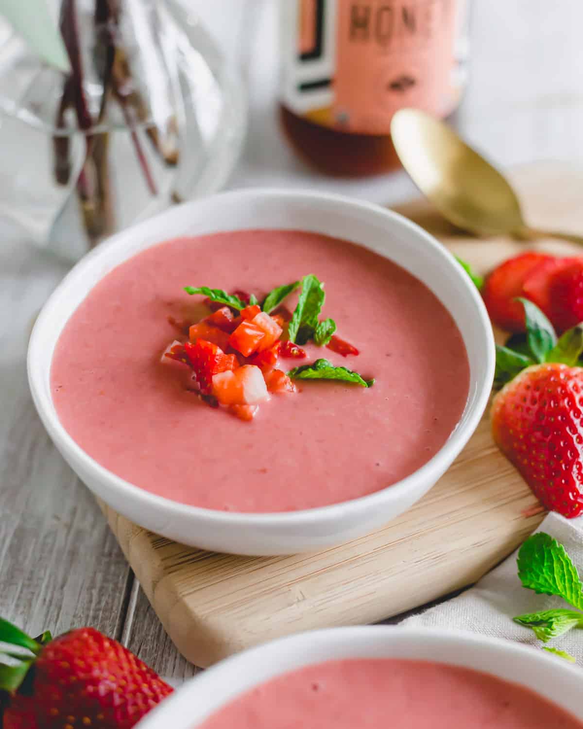 Strawberry gazpacho in a white bowl on a cutting board.