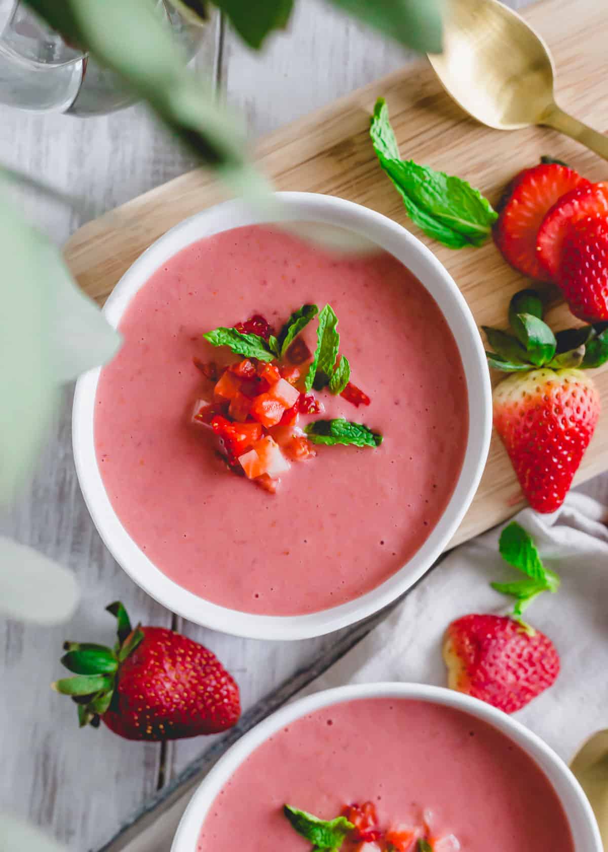 Easy blender cold strawberry soup with strawberry and mint garnish on a white surface.