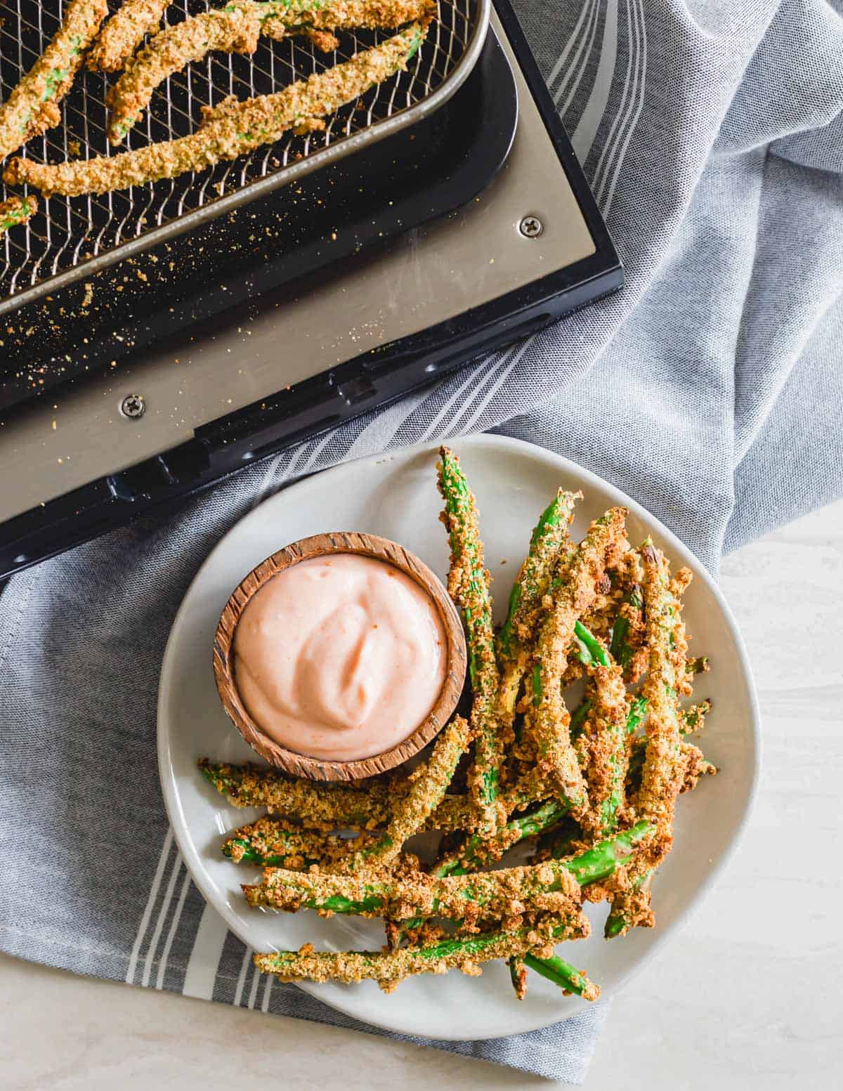 Gluten-free and vegan air fried green bean fries on a plate with dipping sauce and an air fryer in the background.