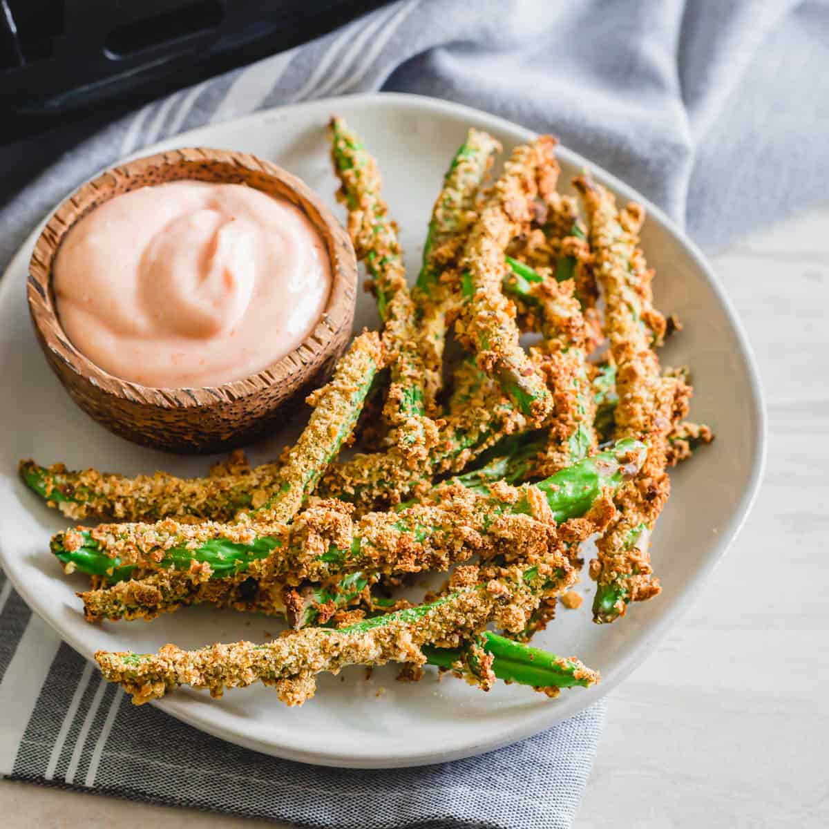 Air fryer green bean fries on a plate with spicy dipping sauce in a small bowl.