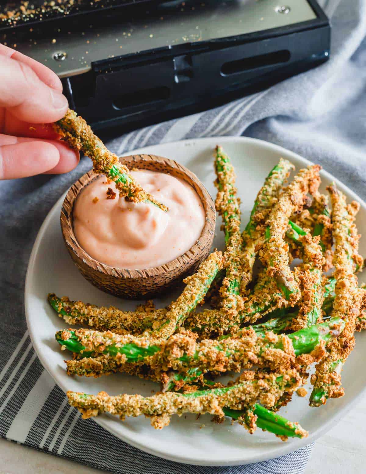 Dipping green bean fries made in the air fryer into a ketchup sriracha sauce.