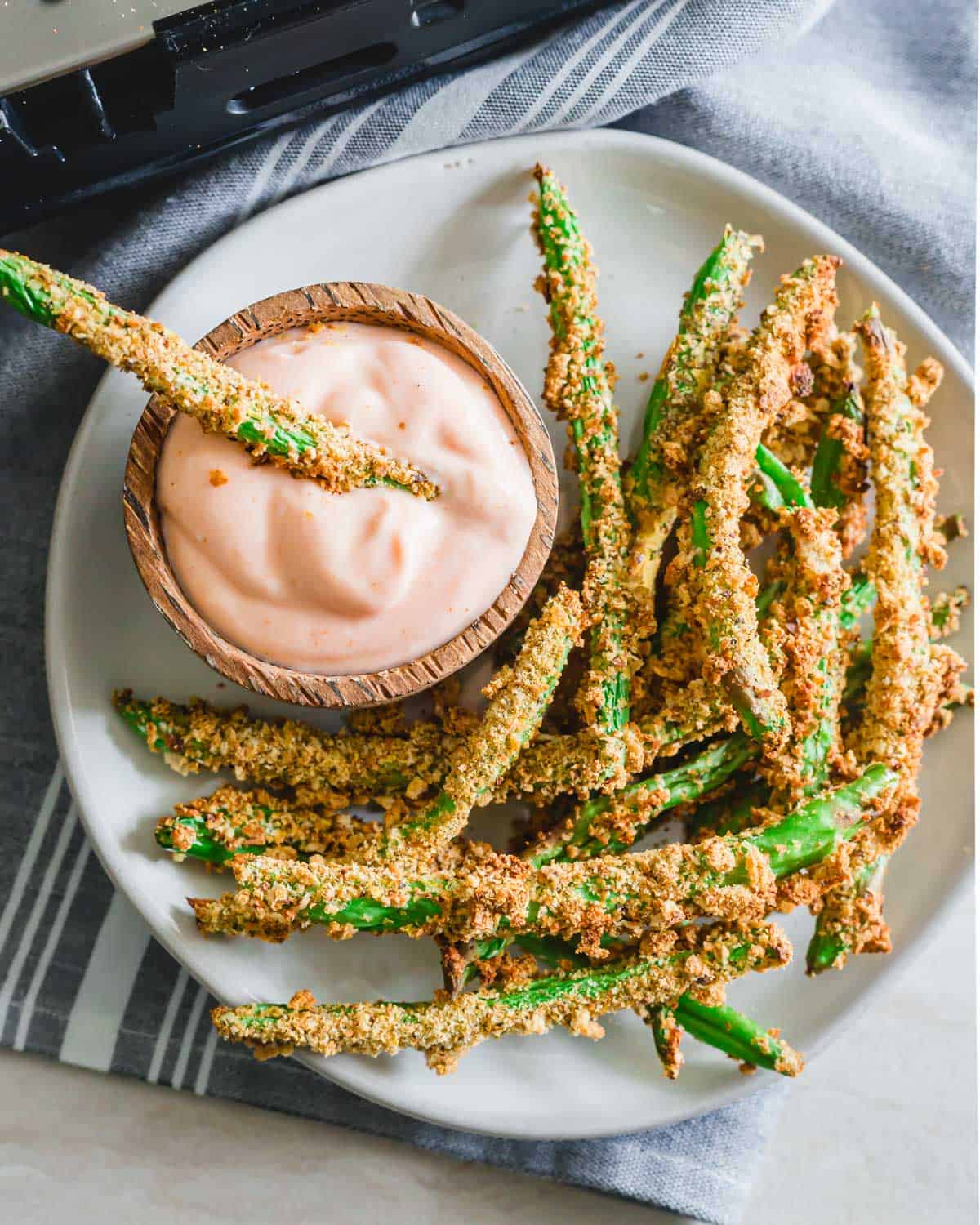Overhead picture of crispy green bean fries on a plate with one in a small bowl of fry sauce.
