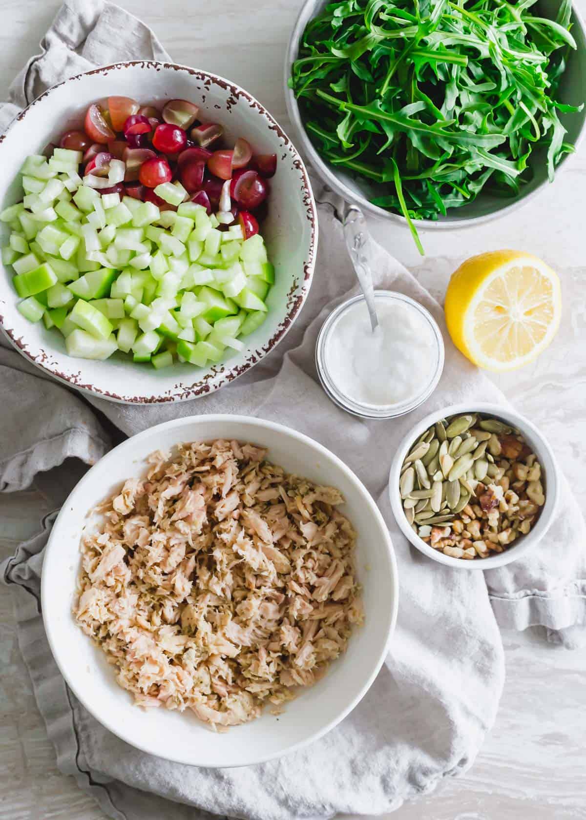 Ingredients to make a tuna Waldorf salad: canned tuna, pepitas, walnuts, apples, celery, yogurt, lemon and red grapes.