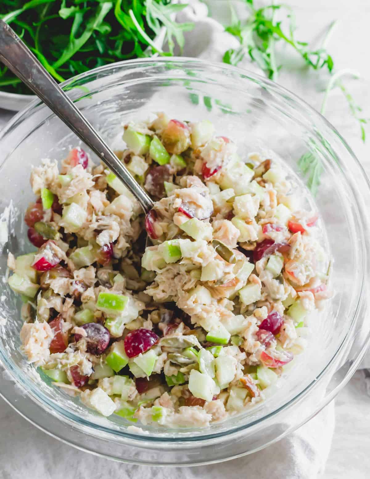 Waldorf salad with tuna recipe in a glass mixing bowl with a spoon.