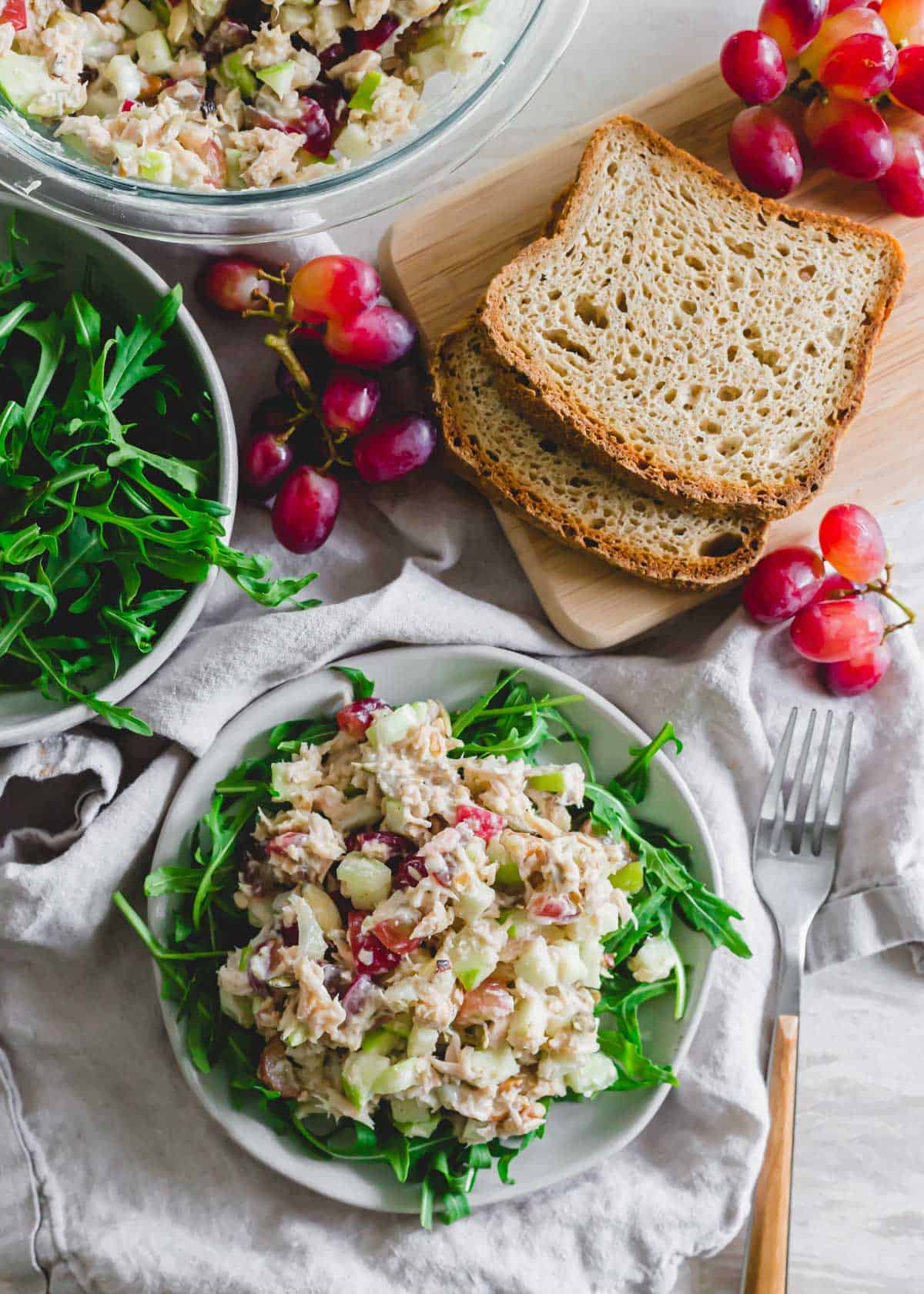 Healthier tuna salad recipe with grapes, celery, apples, walnuts and pepitas with yogurt on top of baby greens on a plate.
