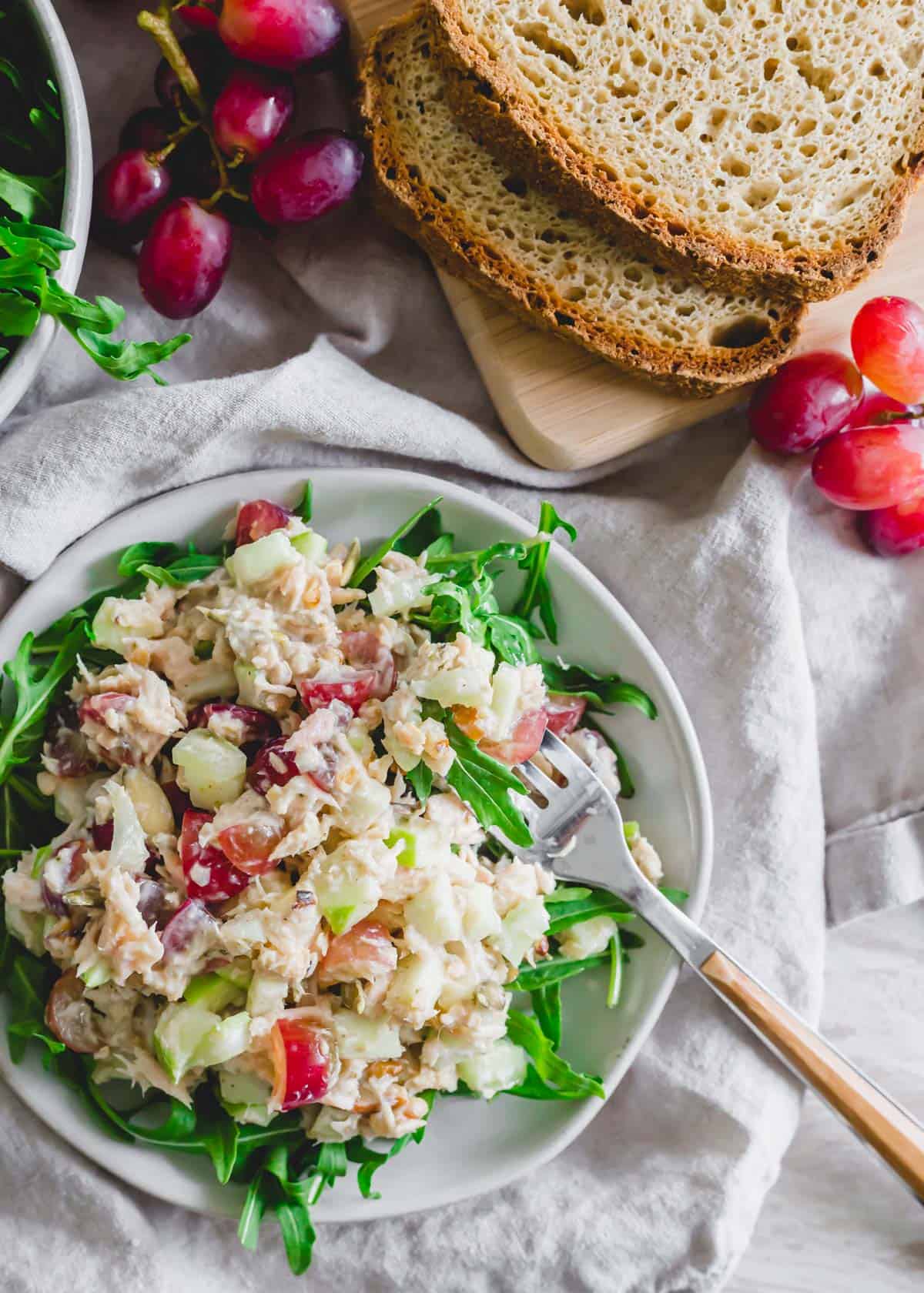 Creamy tuna Waldorf salad recipe served with baby arugula on a plate with a fork.