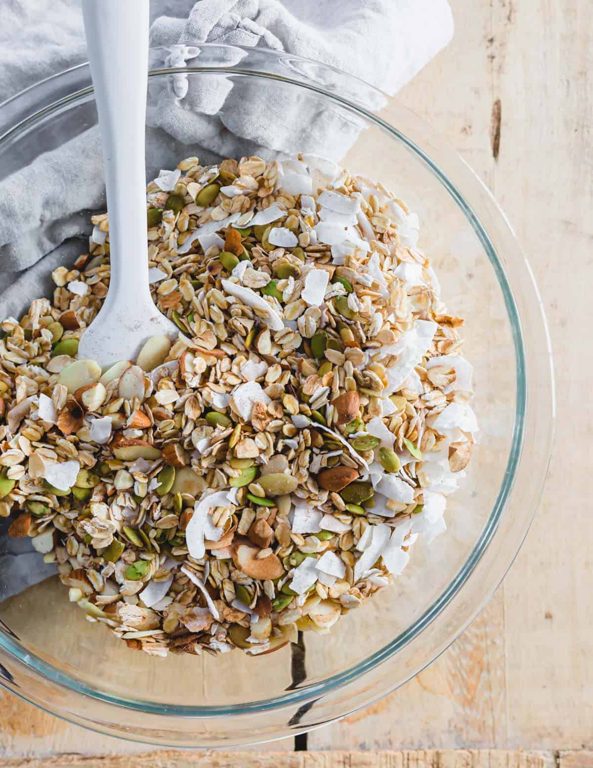 Dry ingredients to make homemade coconut almond granola in a large glass bowl with white spatula.