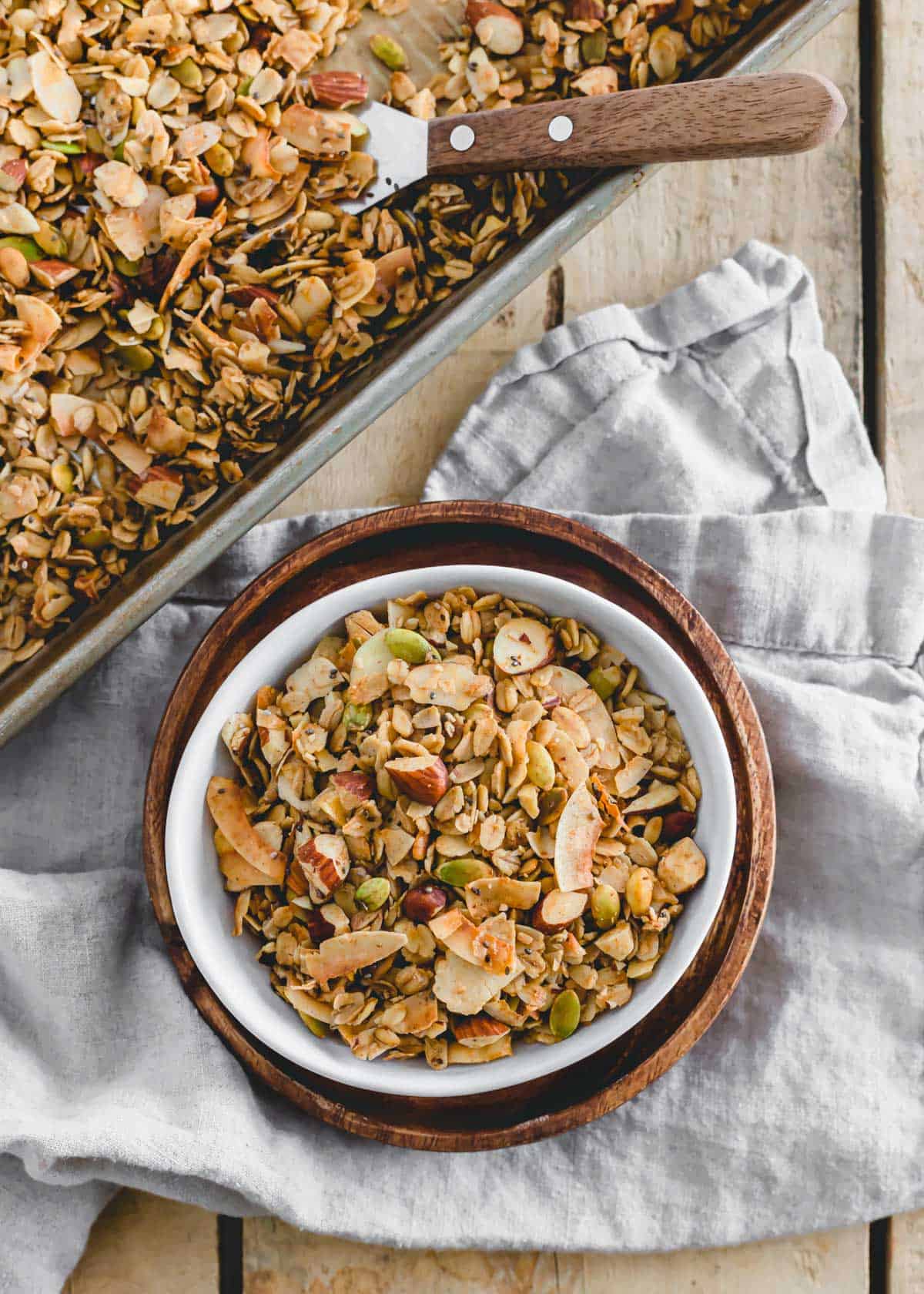 Recipe to make homemade vegan granola with coconut and almonds in a white bowl on a wooden plate.