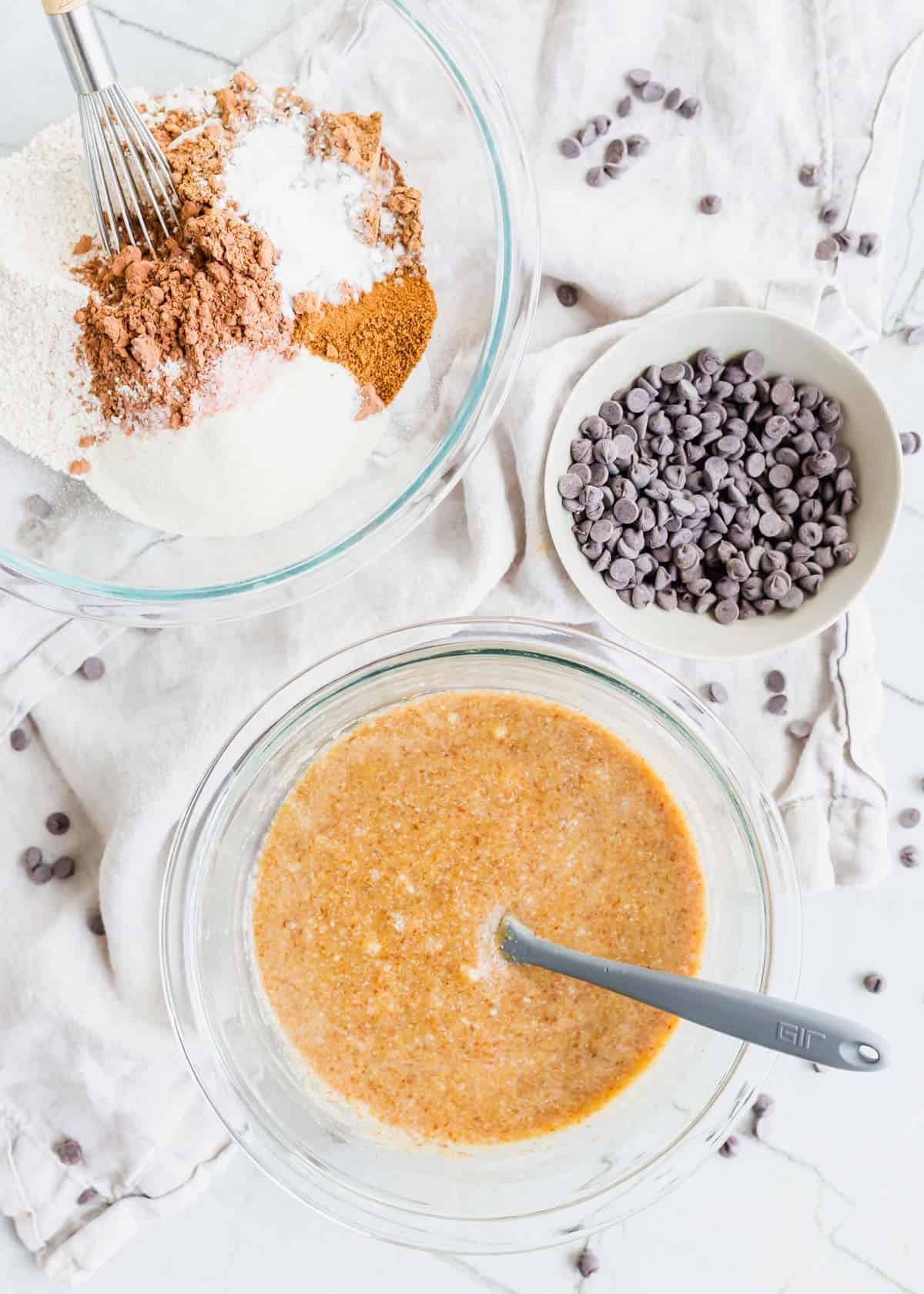 Dry ingredients to make chocolate banana bread in a glass bowl, chocolate chips in a small ceramic bowl and wet ingredients in another glass bowl.