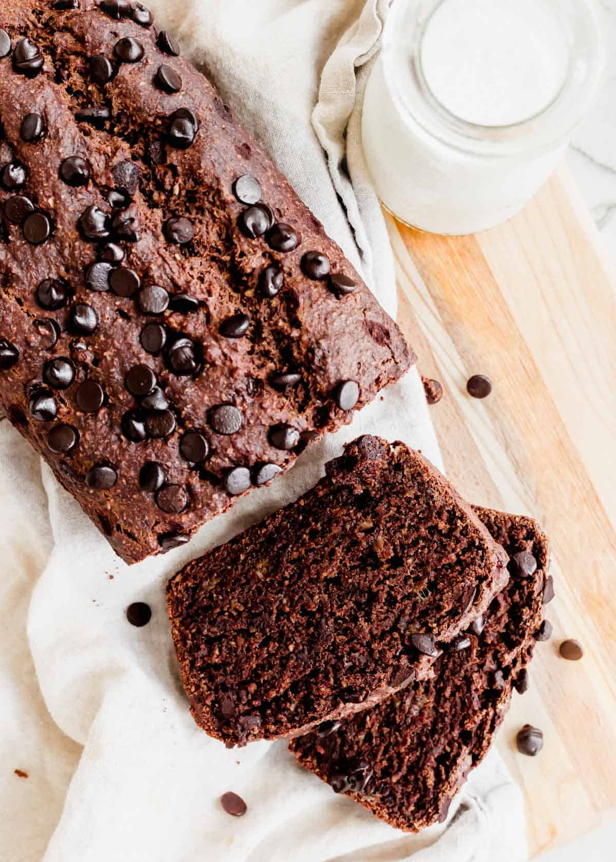 A loaf of double chocolate banana bread with two slices cut on a wooden cutting board.