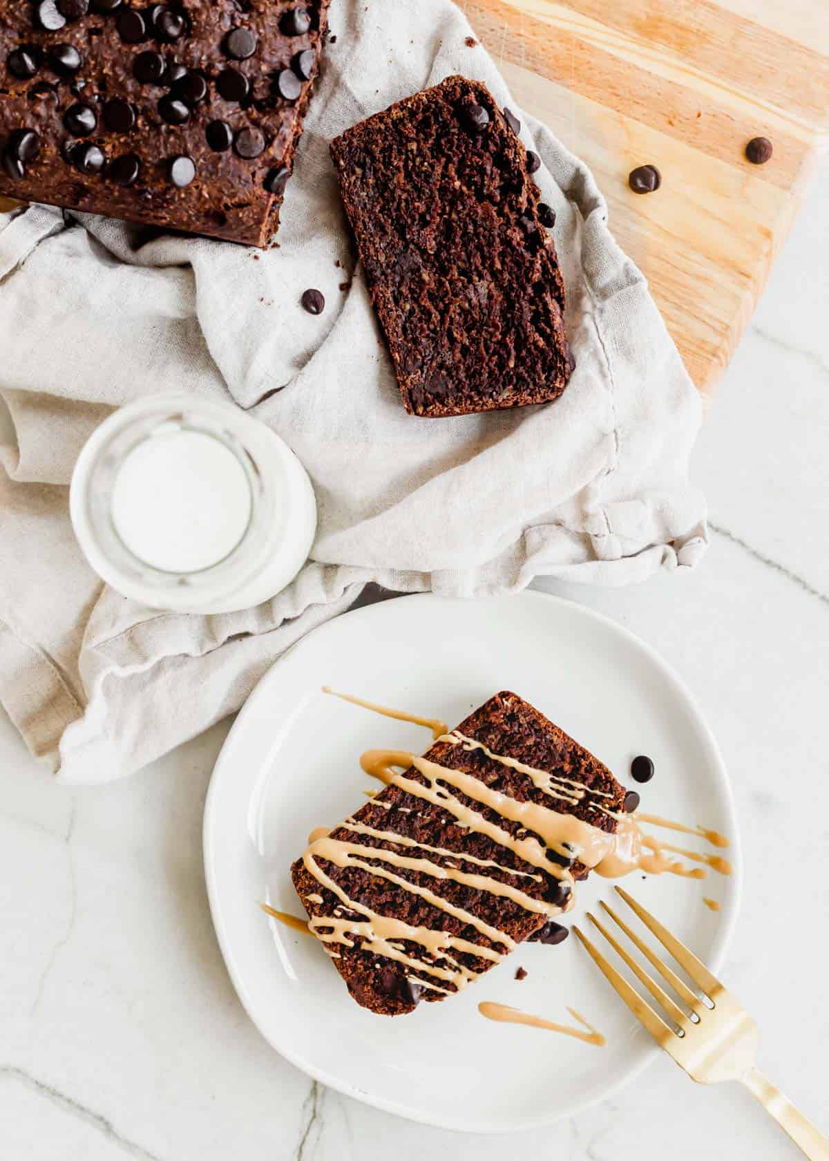 Slice of gluten-free and vegan chocolate banana bread with chocolate chips drizzled in peanut butter on a plate with a fork.