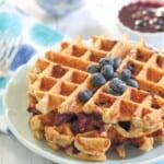 Stacked oatmeal waffles on a blue plate with blueberries.