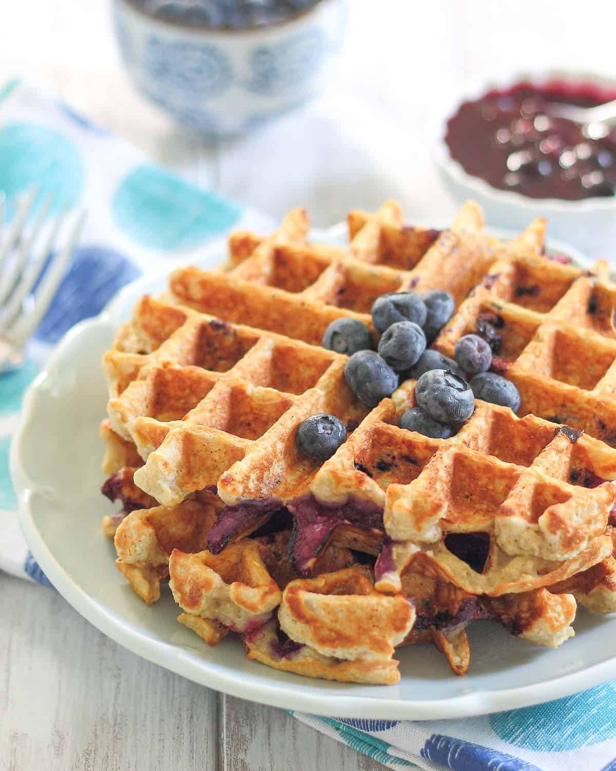 Stacked oatmeal waffles on a blue plate with blueberries.