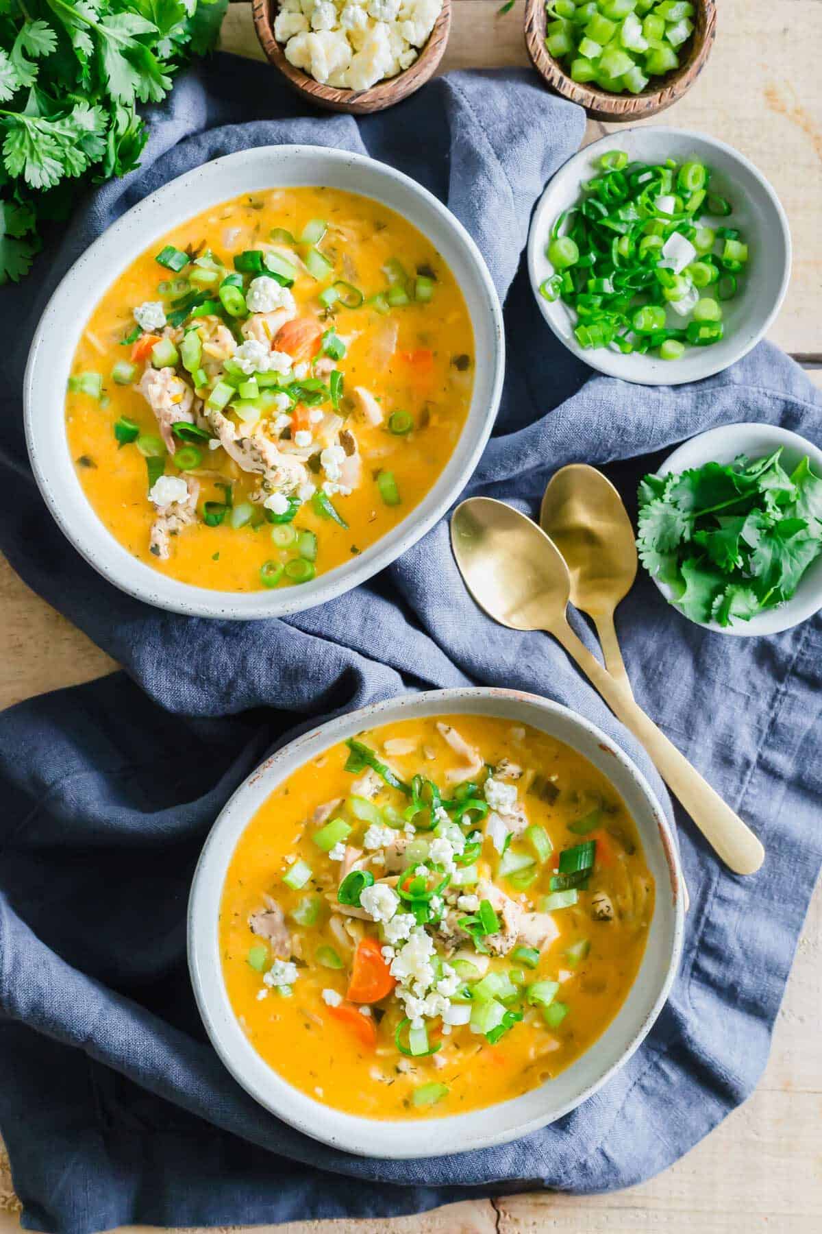 Buffalo chicken wing soup in bowls with garnishes on the side.