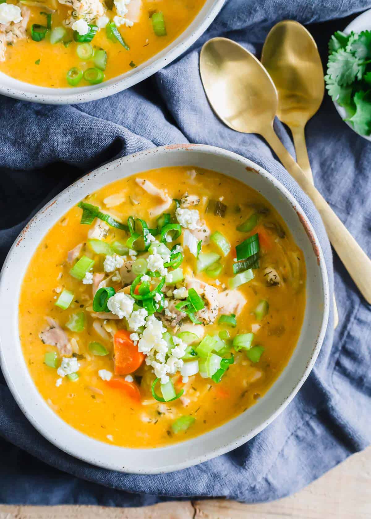 Spicy buffalo chicken soup in a bowl topped with scallions, blue cheese crumbles, celery and cilantro.