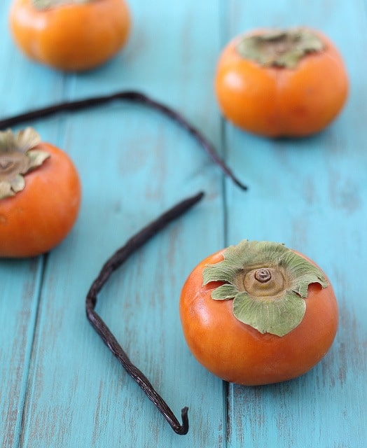 Four whole hachiya persimmons on a wooden countertop.