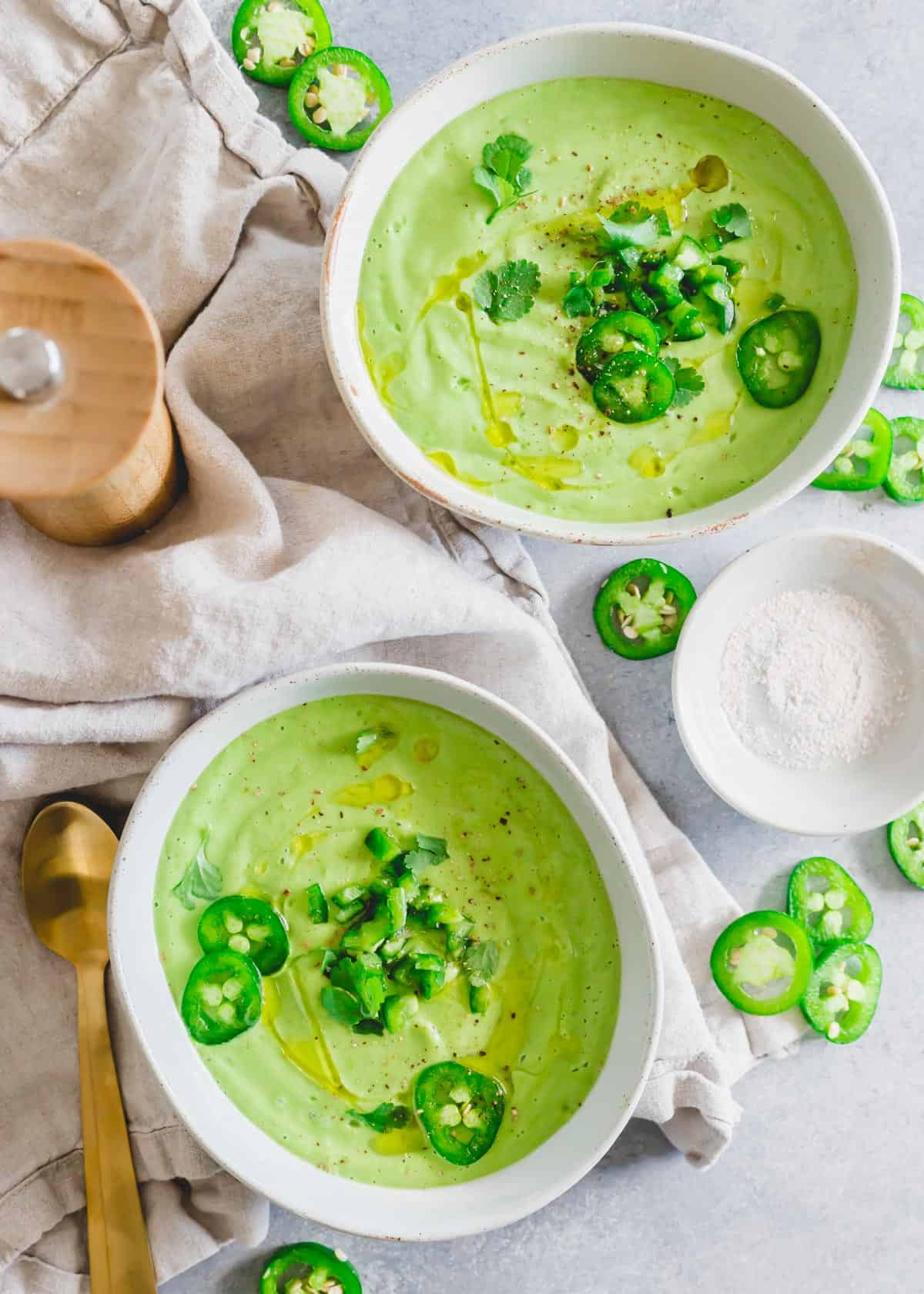 Cold avocado soup in bowls garnished with jalapeño and cilantro. 