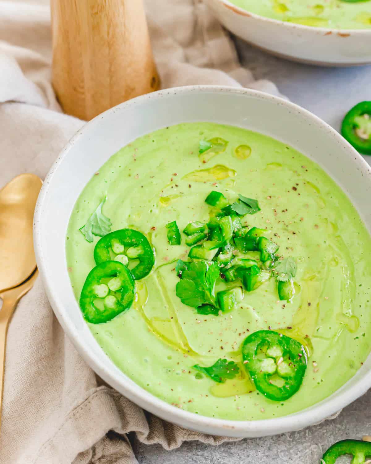 Avocado gazpacho made in the blender in a bowl with spoons on the side.