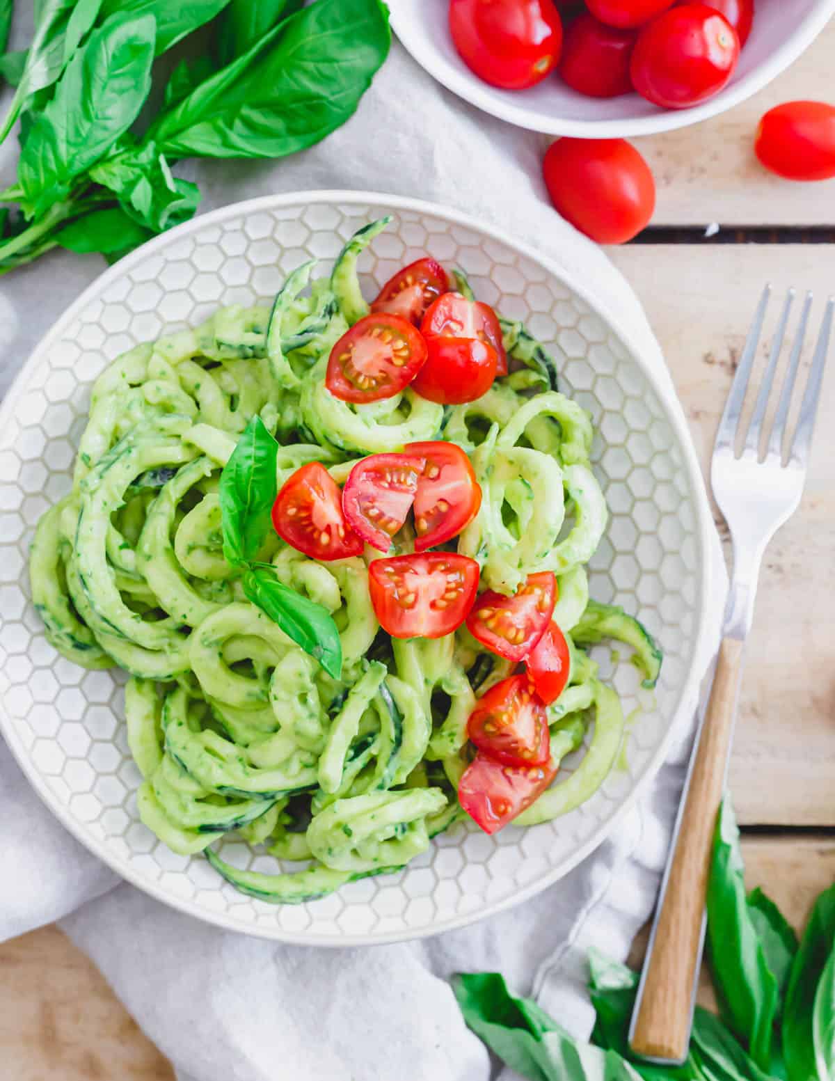 Zucchini noodle pasta with creamy avocado sauce and cherry tomatoes in a bowl.