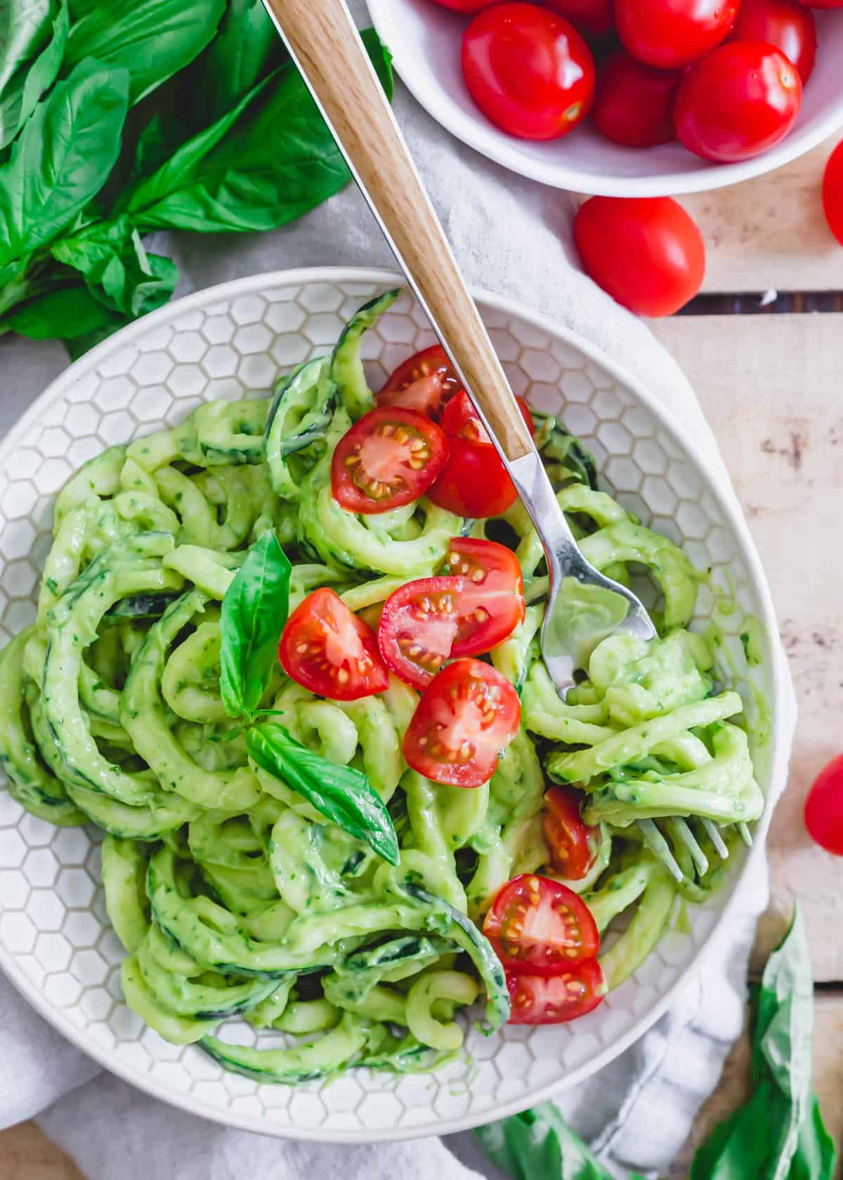 Zoodles tossed with avocado cream sauce and served with cherry tomatoes in a bowl with a fork.