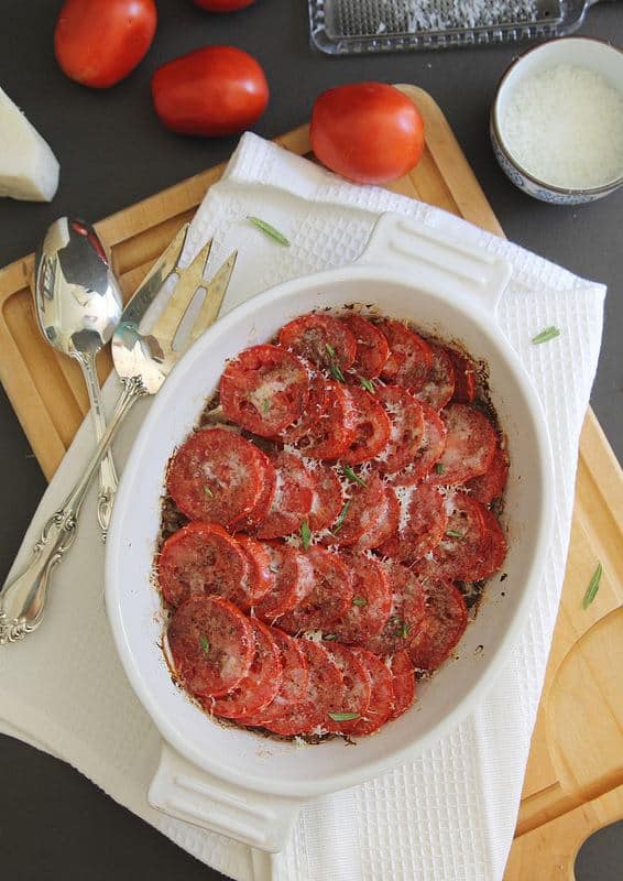 Fresh tomato gratin with parmesan cheese in a baking dish on a cutting board.
