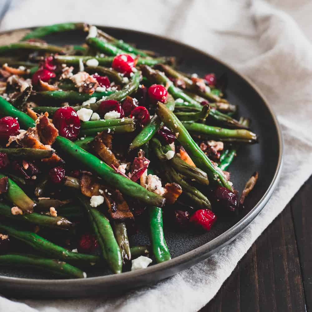 Green beans with bacon, cranberries and goat cheese on a plate.