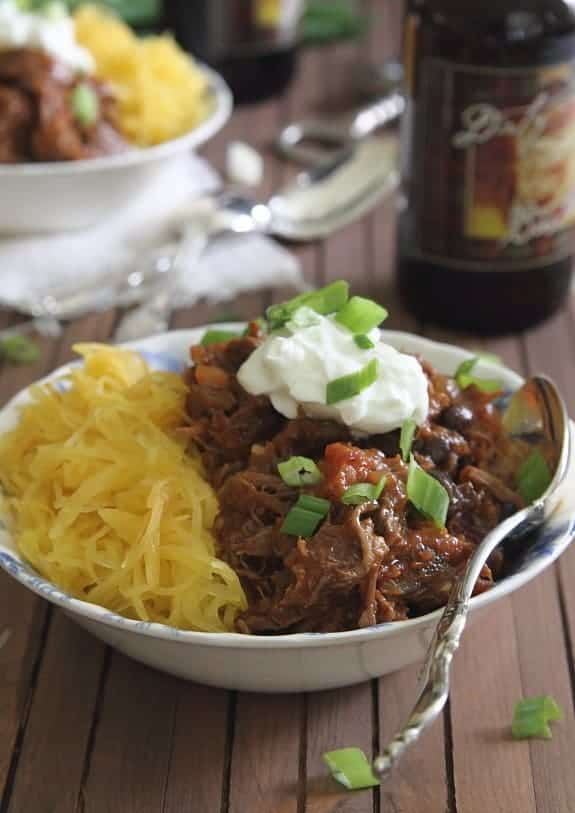 Short rib chili in a white bowl with a spoon topped with sour cream
