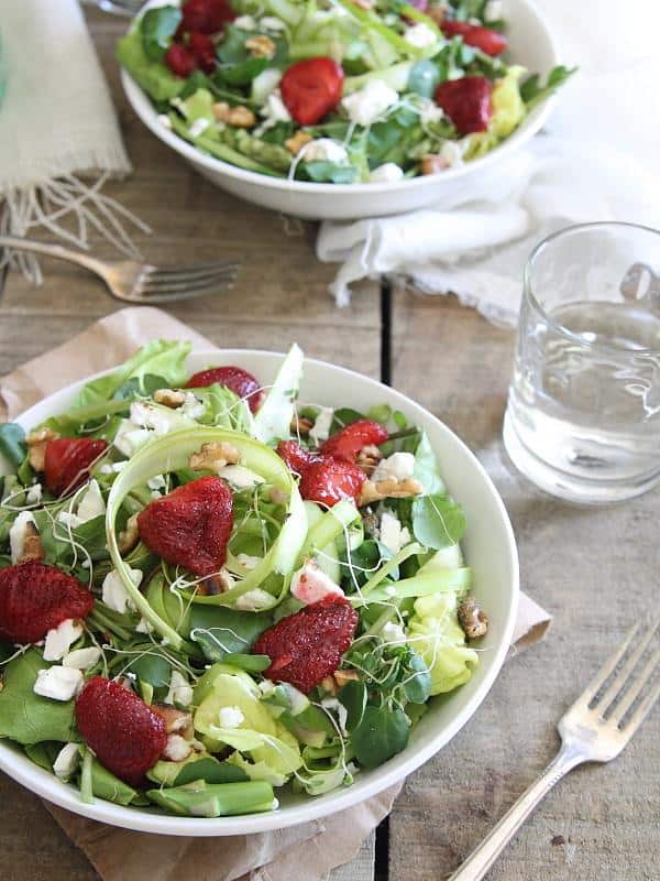 Fresh strawberry feta salad in a white bowl next to a fork and glass.
