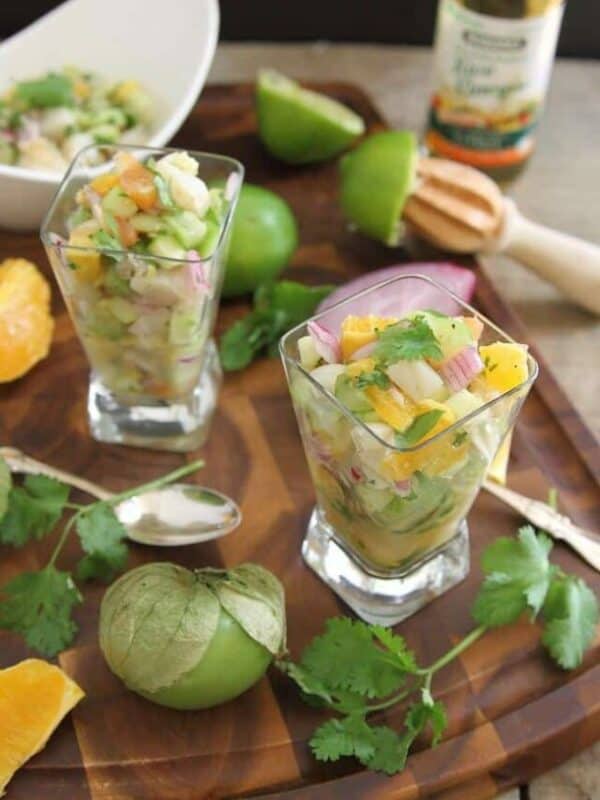 Two glasses of fruit salad on a wooden cutting board.