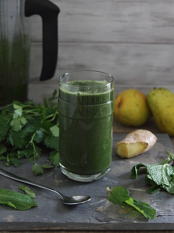 Detox Green Smoothie in a glass next to a spoon and green veggies.